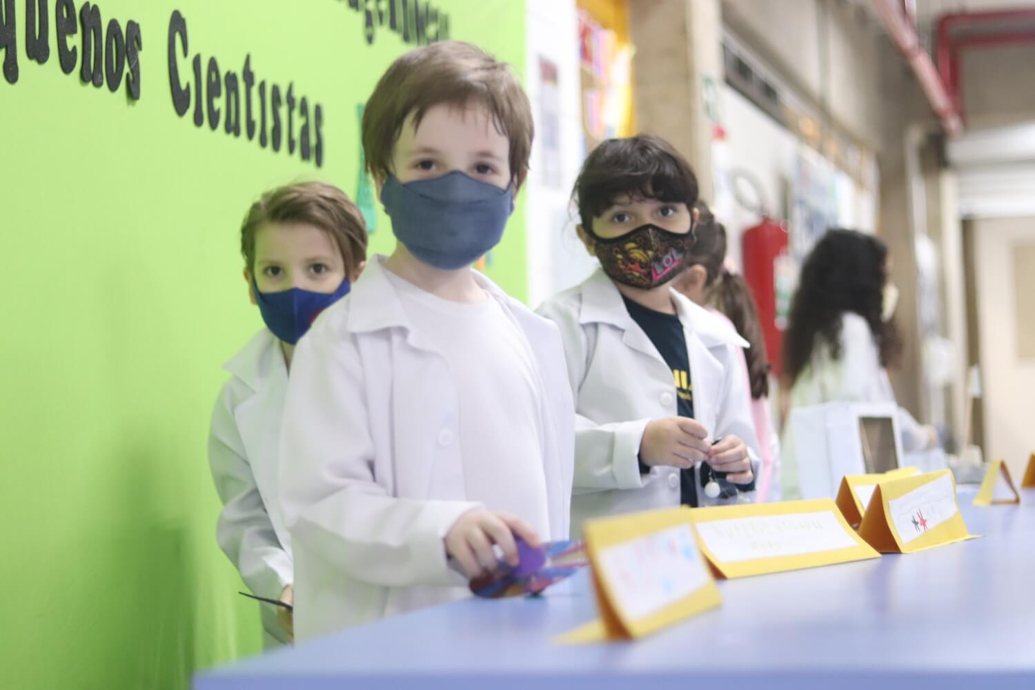 Três crianças com avental de cientista olhando para a câmera