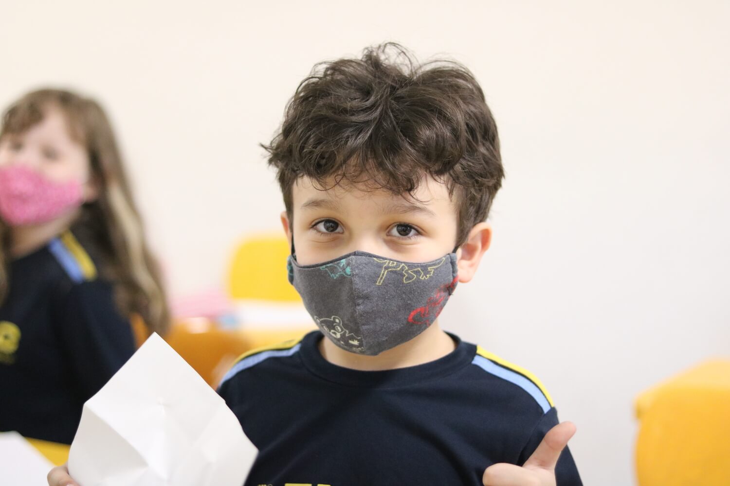 Criança de máscara fazendo o sinal de jóia