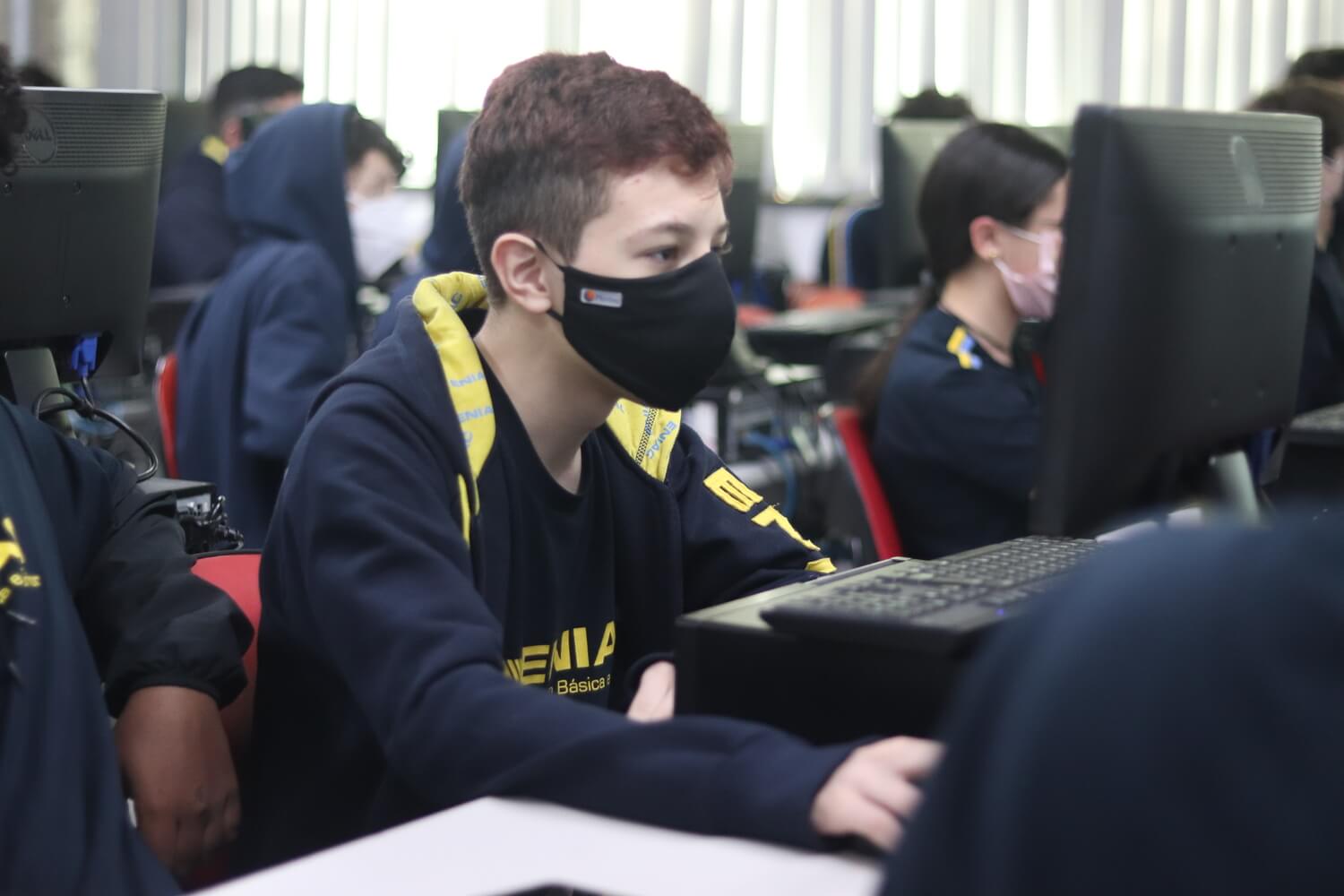 Menino de máscara usando o computador