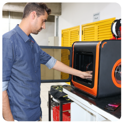 Homem do curso de Engenharia  Mecatrônica do eniac fabricando algo na impressora 3D